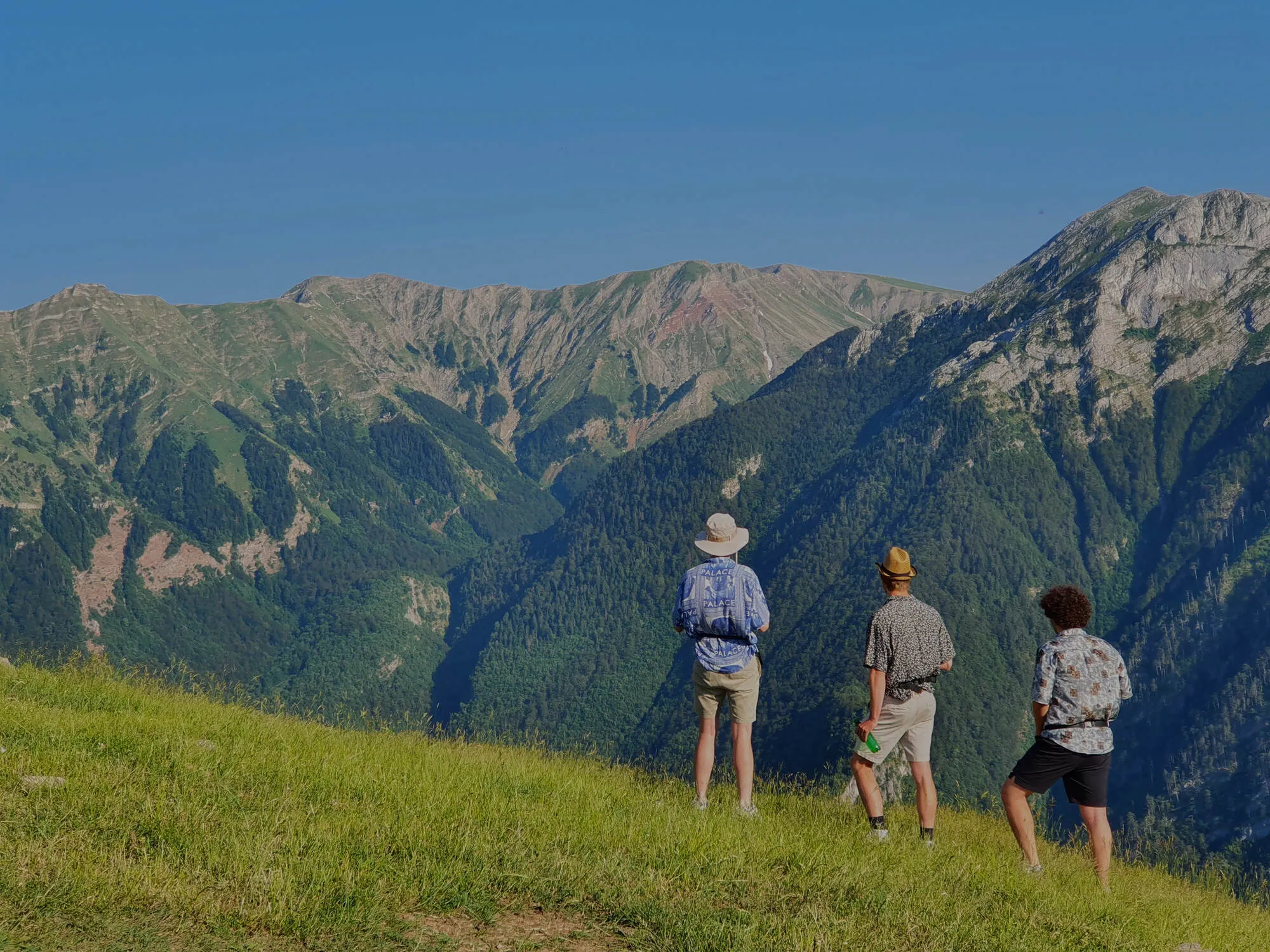 Three hikers standing on a grassy ridge, looking out across the mountains